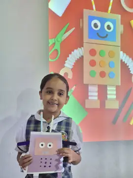 Estudiante con uniforme de diario muestra un robot de papel que construyó en clase
